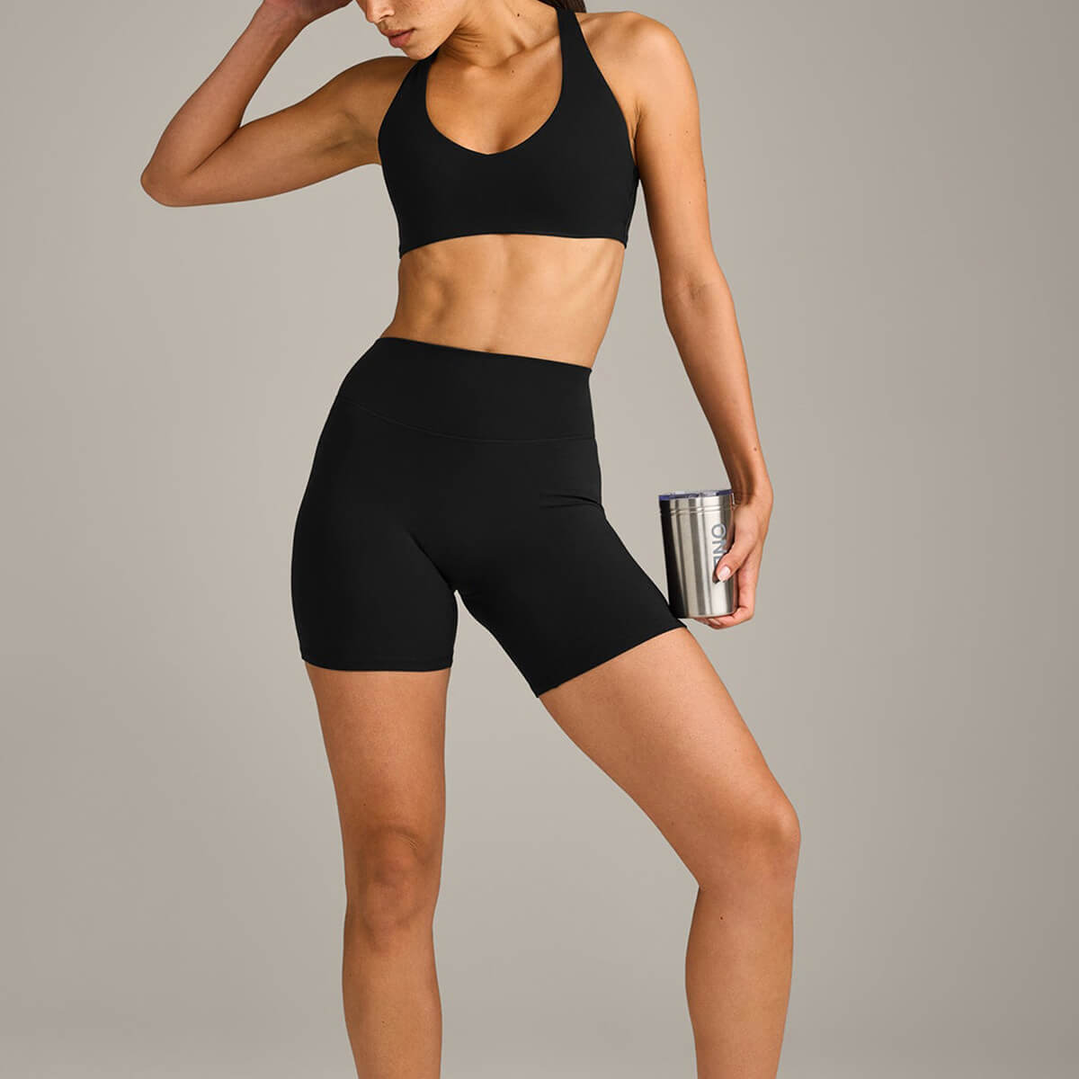 A woman posing in a matching black activewear set including a supportive sports bra and high-waisted biker shorts, holding a water bottle.