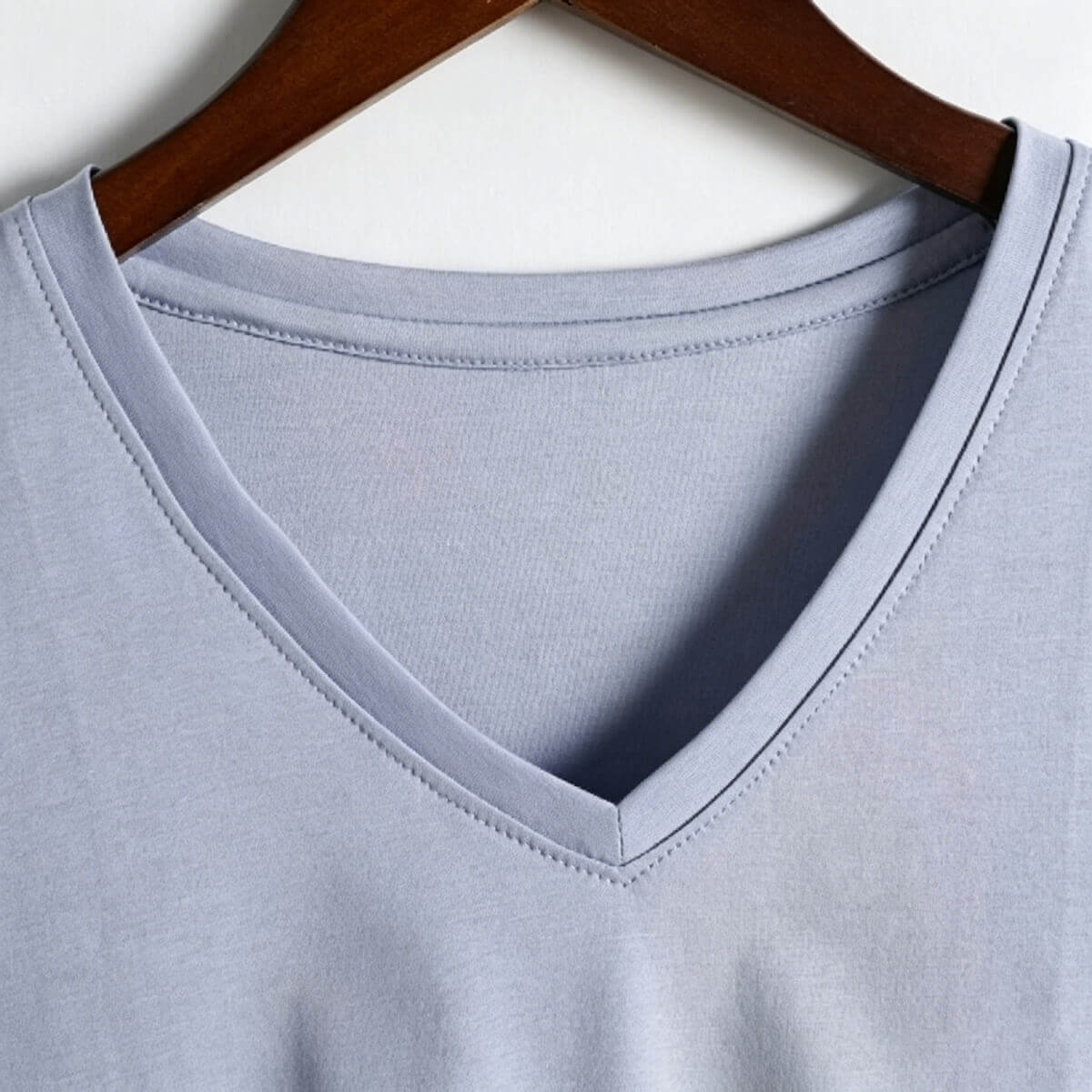 Close-up detail of the sleeve hem and fine stitching on a light blue 80S long-staple cotton T-shirt, showing durable craftsmanship.