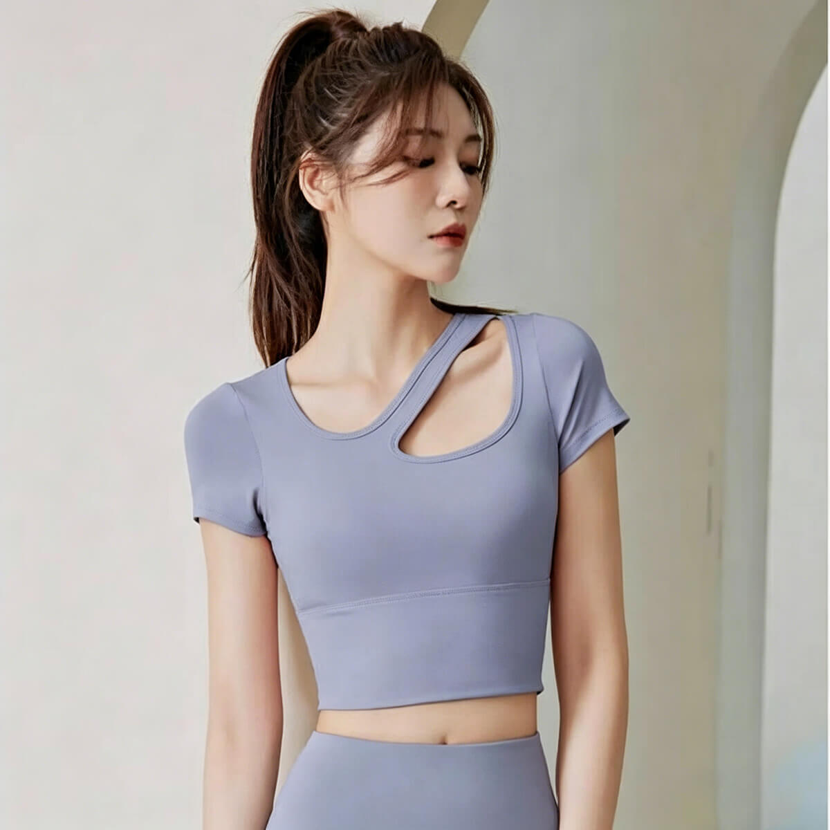 Periwinkle blue sports tee for women featuring a trendy asymmetric keyhole neck and body-hugging silhouette for athleisure wear.