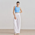 Full body view of a model in an azure blue ribbed high-neck crop tank top paired with flowy white wide-leg trousers.