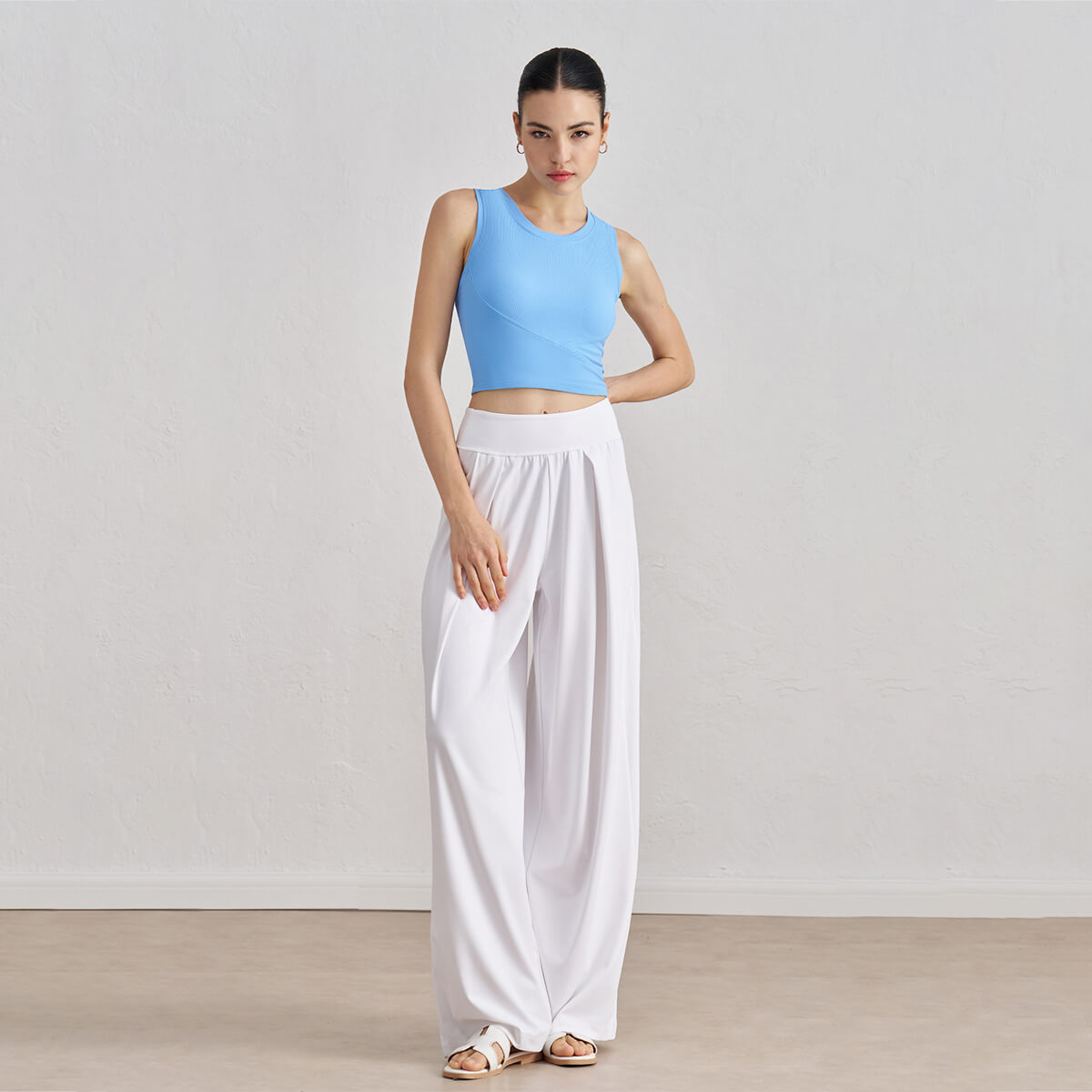 Full body view of a model in an azure blue ribbed high-neck crop tank top paired with flowy white wide-leg trousers.