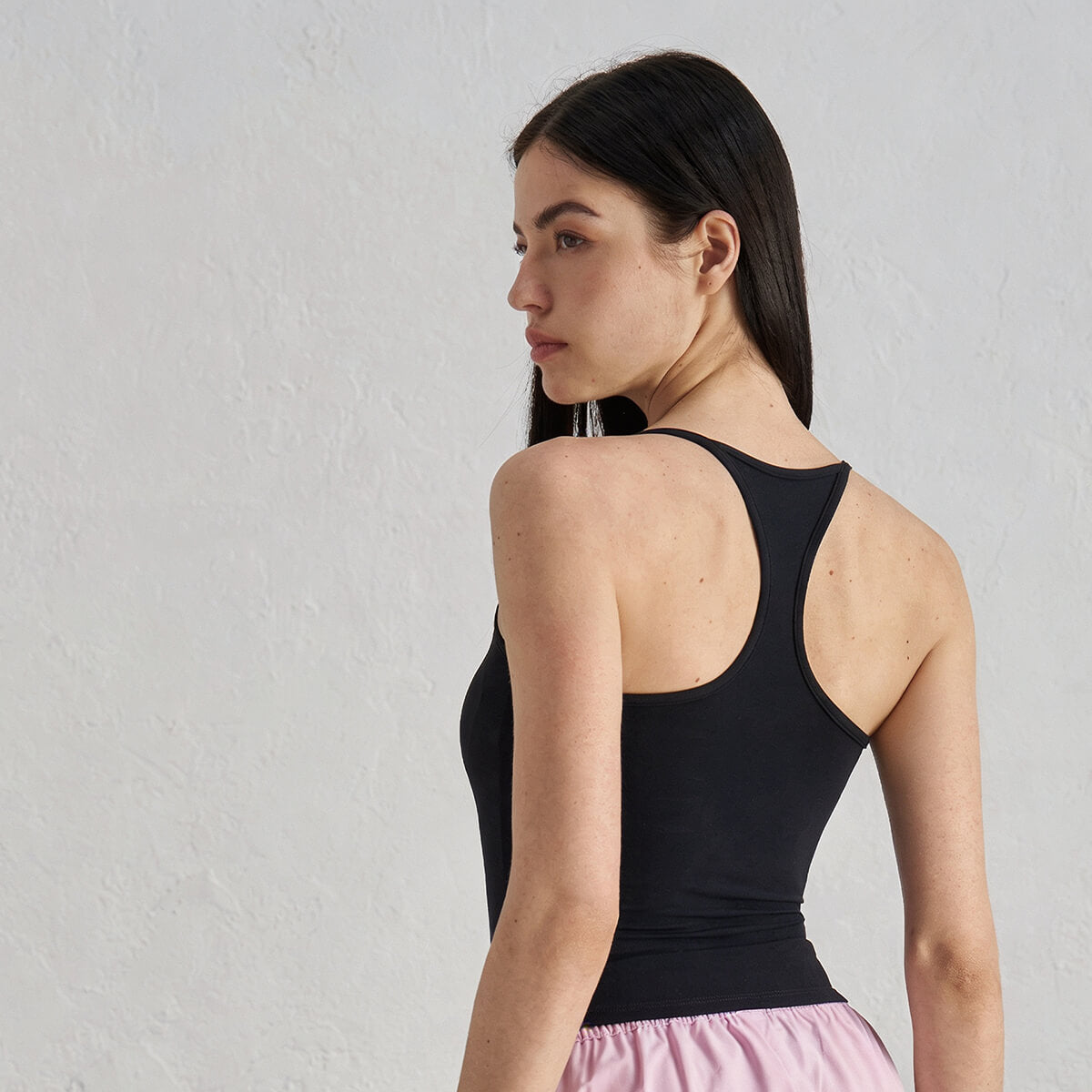 Back view of a woman wearing a classic black activewear racerback tank top paired with pink shorts