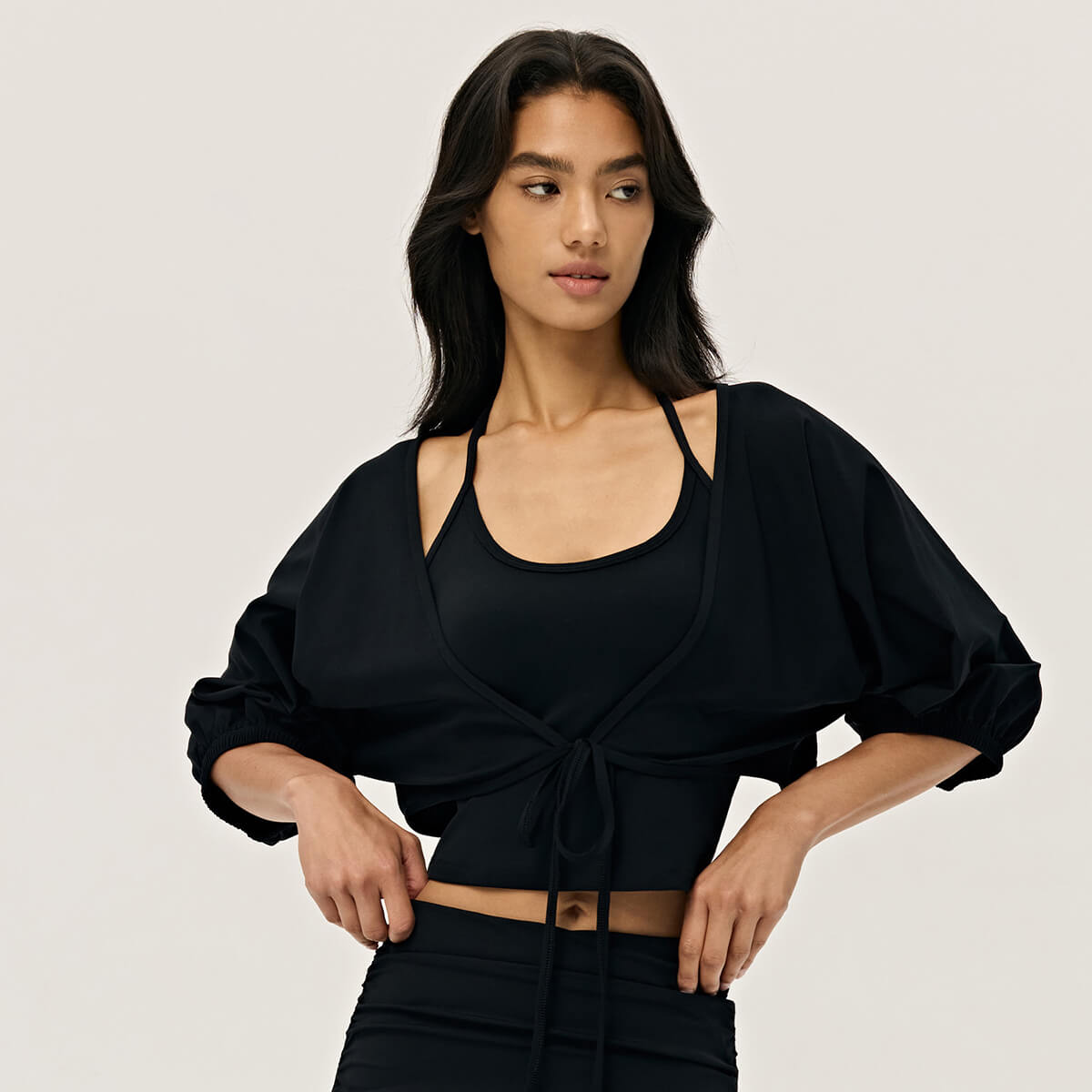A woman wearing a classic black cropped shrug with balloon sleeves, perfect for a chic athleisure look.