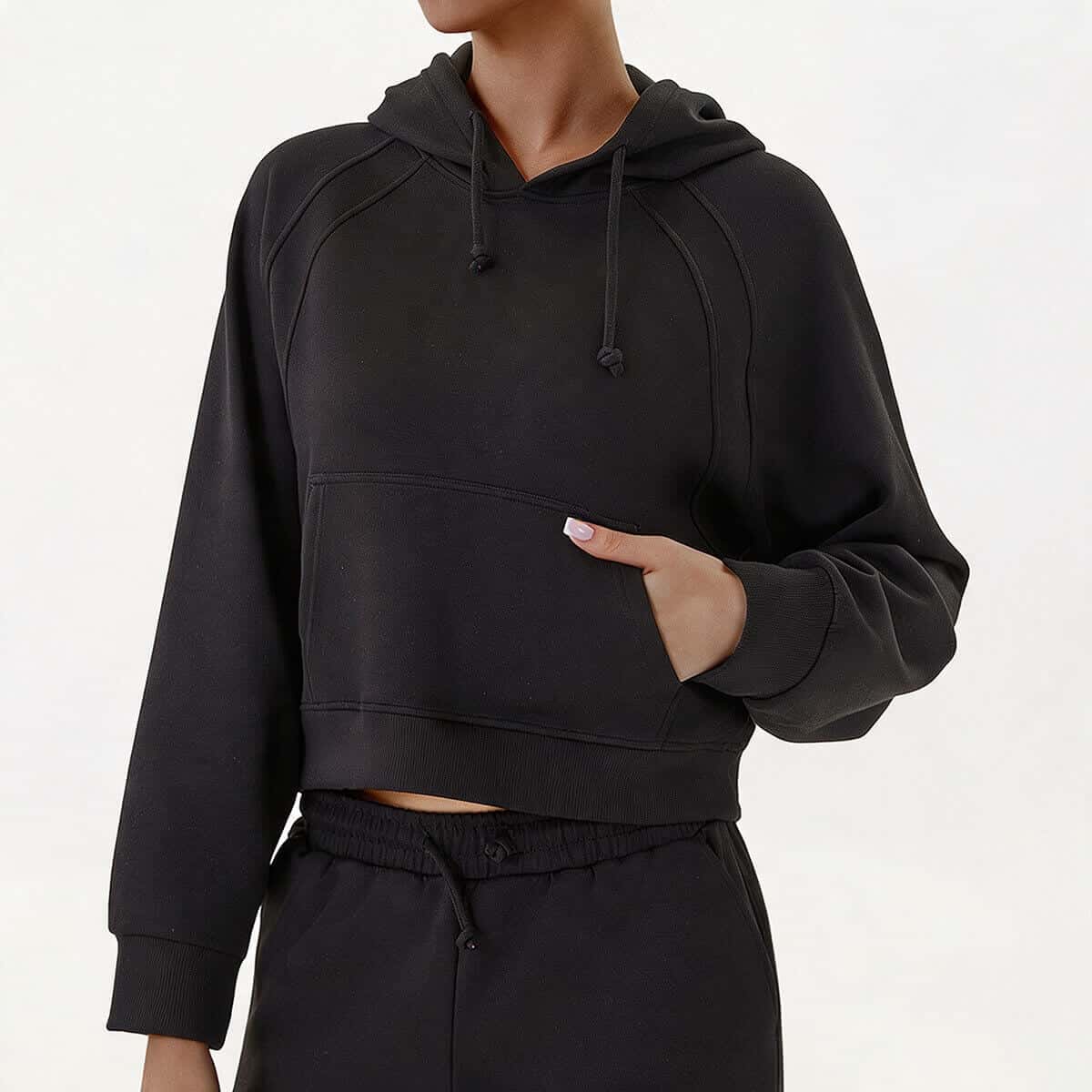 A woman wearing a classic black cropped pullover hoodie with a functional kangaroo pocket and matching joggers for a sleek athleisure look.