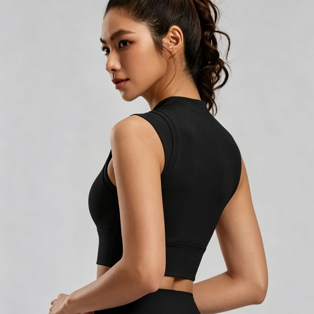 Side-back view of a sleeveless black mock neck activewear crop top highlighting the smooth full-coverage back and sleek athletic silhouette