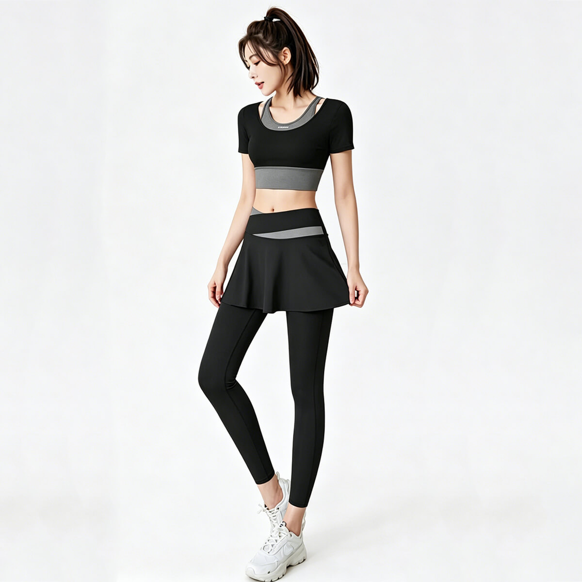 Model wearing a black skirted leggings set with a matching cropped top, featuring grey contrast waistband details for a professional gym look