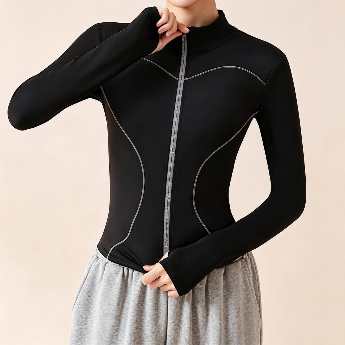 A model wearing a black slim-fit gym jacket with thumbholes and contrast stitching, styled with grey sweatpants for a workout outfit.