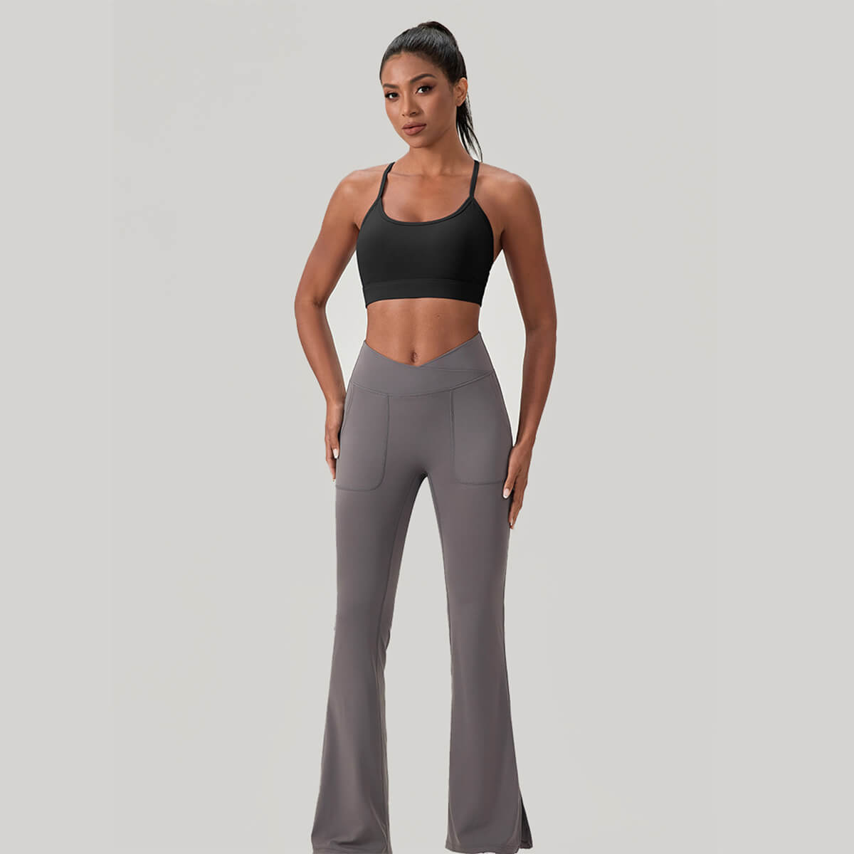 Full body shot of a fitness model in a black sports bra paired with grey high-waisted crossover flare yoga pants.
