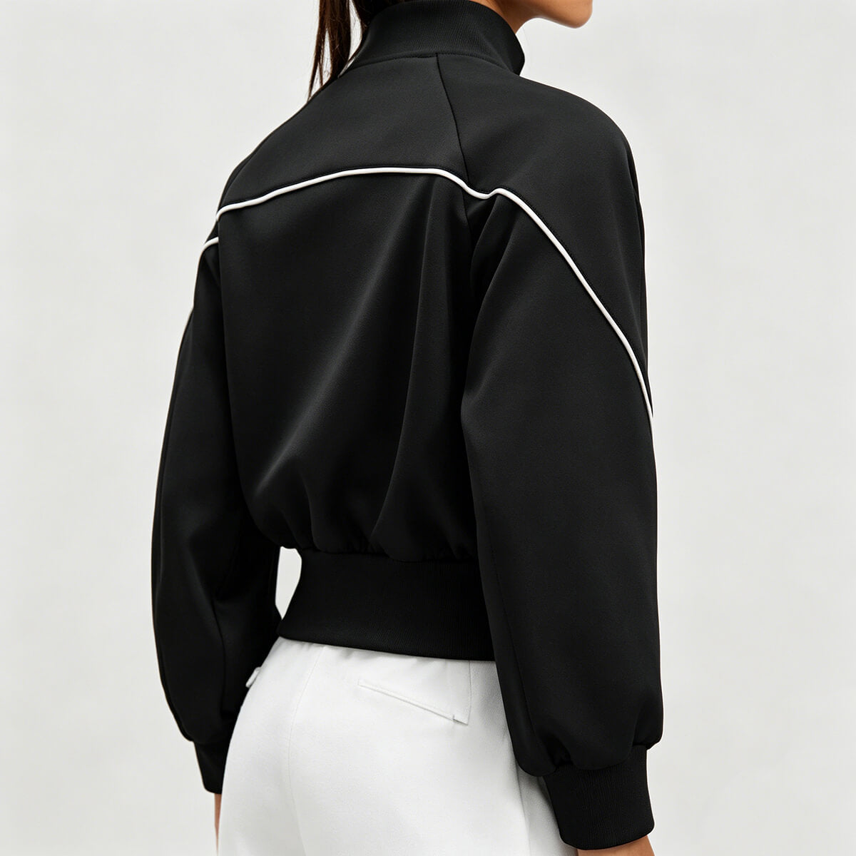 Back view of a black gym track jacket for women showing unique white curved piping detail and high-neck stand collar design.