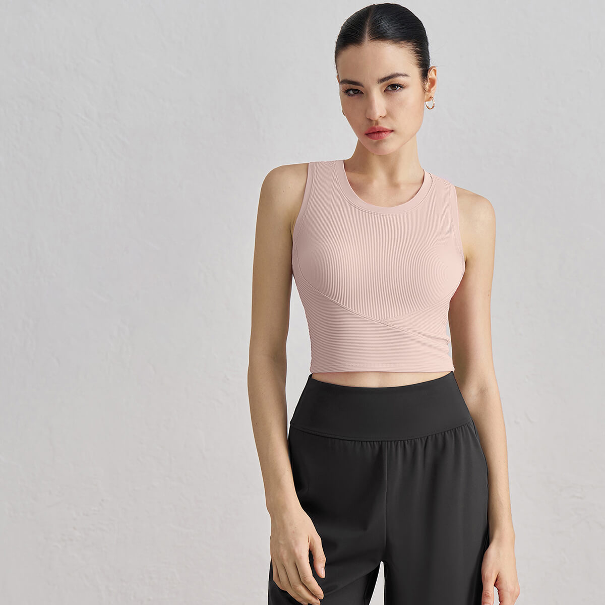 A woman wearing a blush pink ribbed high-neck cropped tank top, ideal for studio-to-street styling.