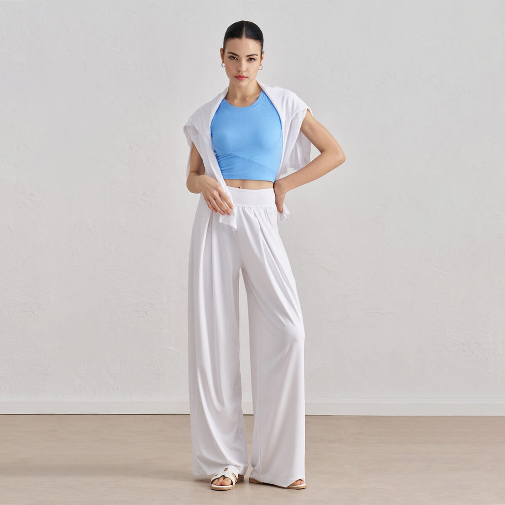 A stylish athleisure look featuring a bright blue ribbed cropped tank top and white wide-leg pants with a shirt draped over shoulders.