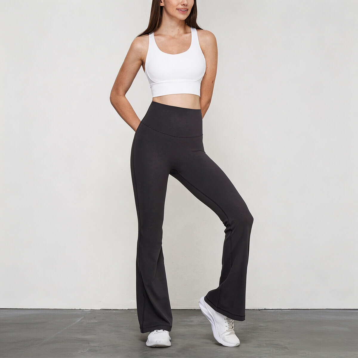 Full body front view of a model in charcoal gray flare yoga pants and a white sports bra, perfect for studio-to-street wear.