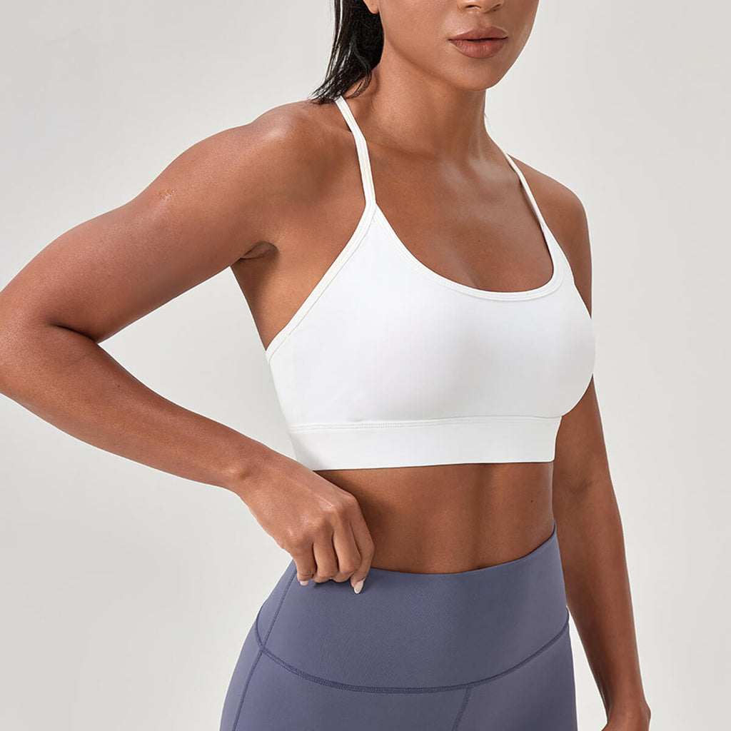 A clean, minimalist white sports bra with a scoop neck and thin racerback straps, styled with navy blue leggings.
