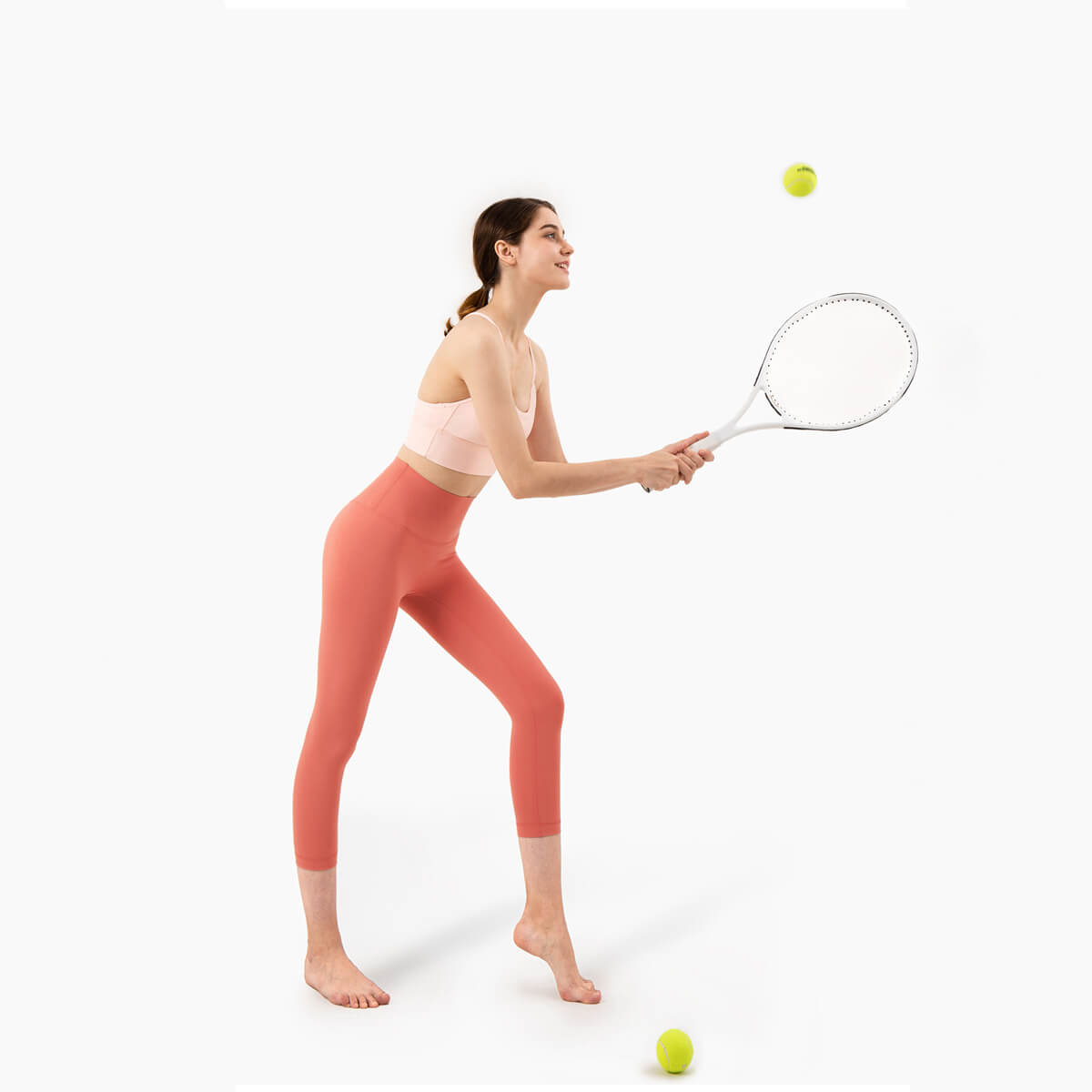 A woman playing tennis while wearing coral capri leggings and a matching sports bra for an active look.