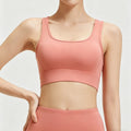 Front view of a women's coral pink scoop neck sports bra featuring wide supportive straps and a seamless finish for yoga and fitness