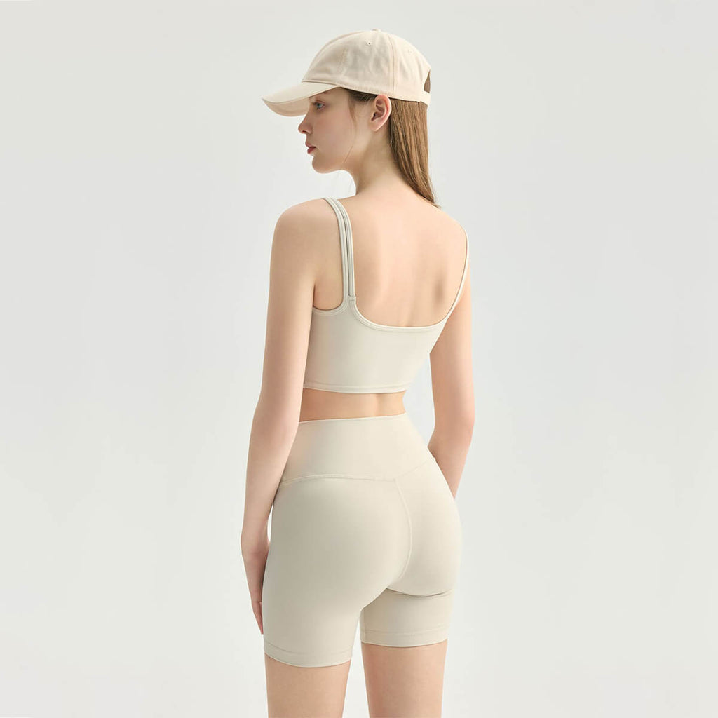 Back view of a woman wearing a cream slim-fit athletic crop top and high-waisted shorts, showing the clean square back design.