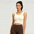 Front view of a woman wearing a cream-colored square neck longline sports bra with wide shoulder straps for yoga and fitness