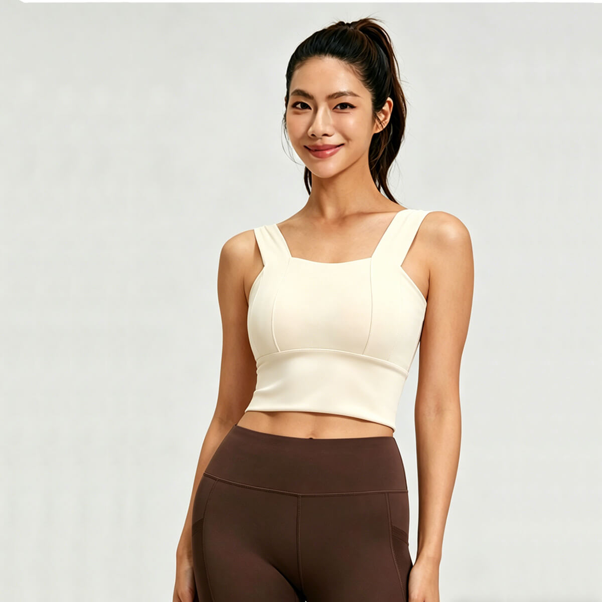 Front view of a woman wearing a cream-colored square neck longline sports bra with wide shoulder straps for yoga and fitness