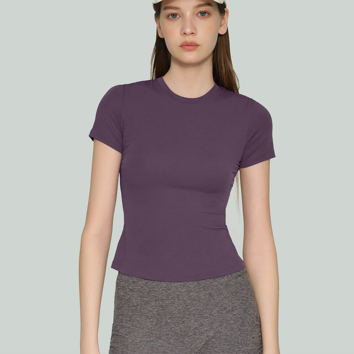 Front view of a dark purple short-sleeve fitness top on a model wearing a matching beige baseball cap.