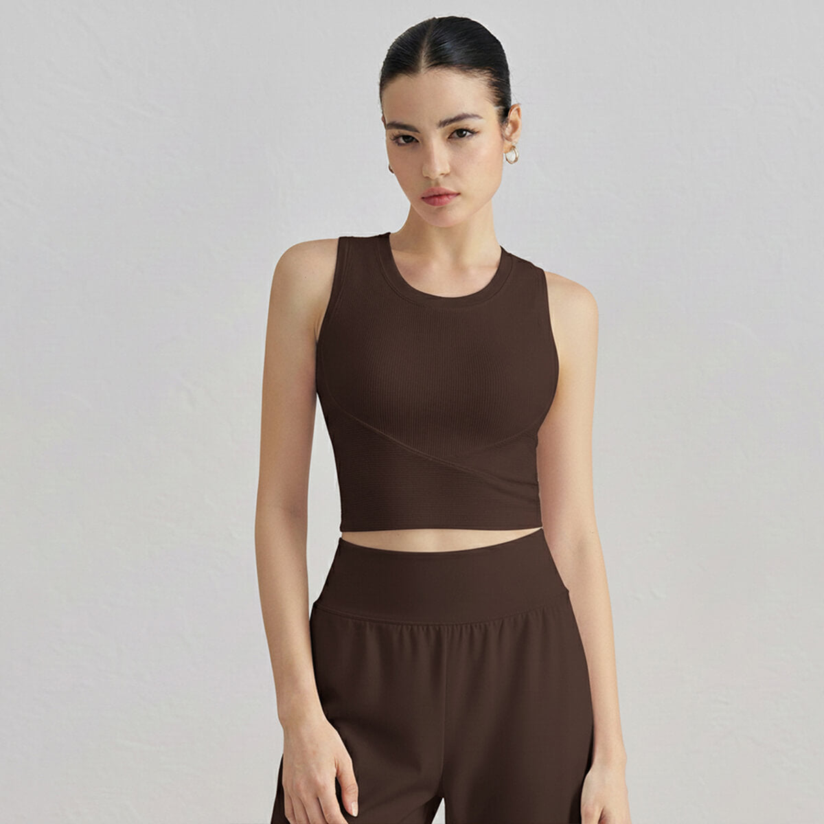 A woman in an espresso brown ribbed high-neck workout crop top paired with matching high-waisted bottoms.