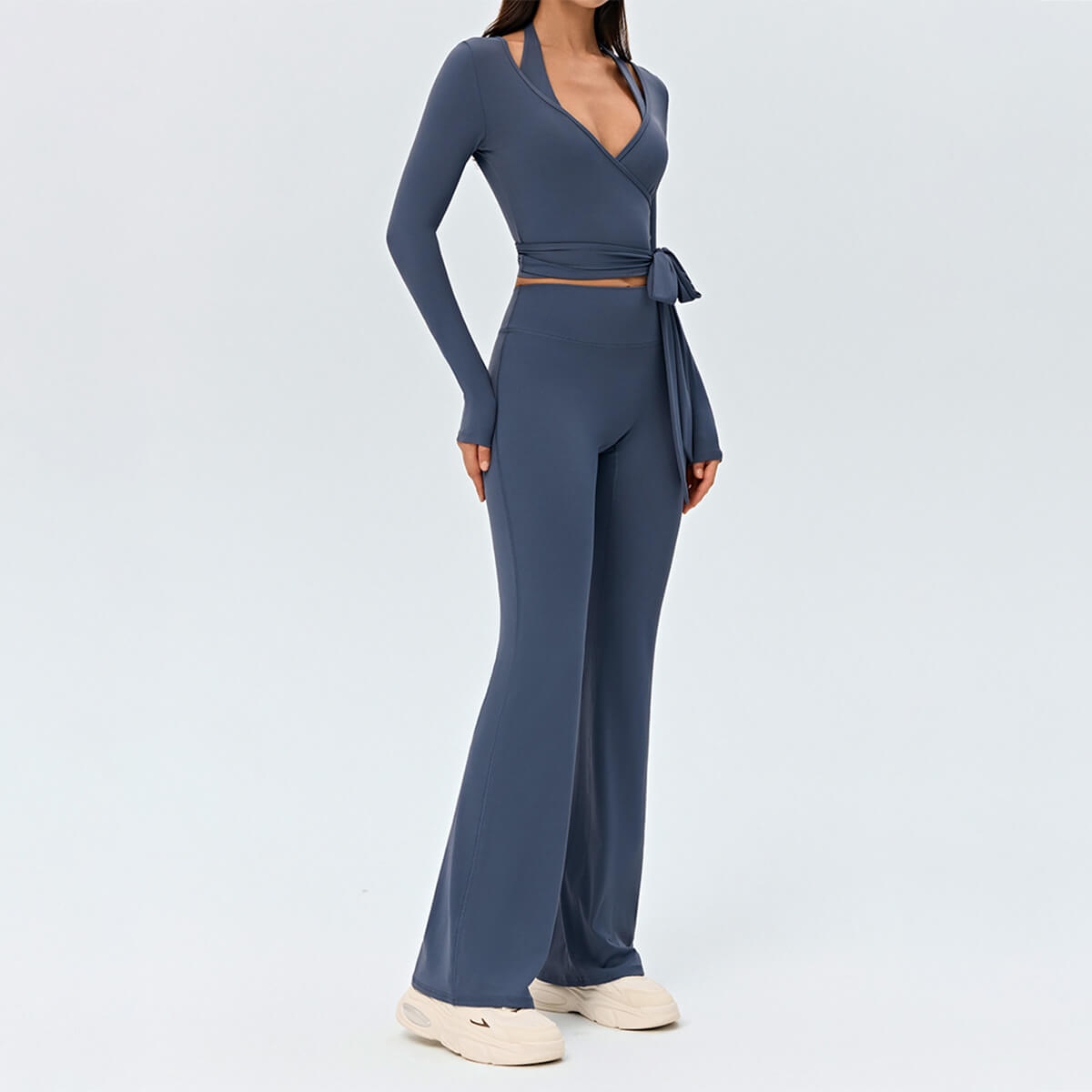 Full-body profile view of a model in a slate blue wrap top and flare leggings yoga set with sneakers.