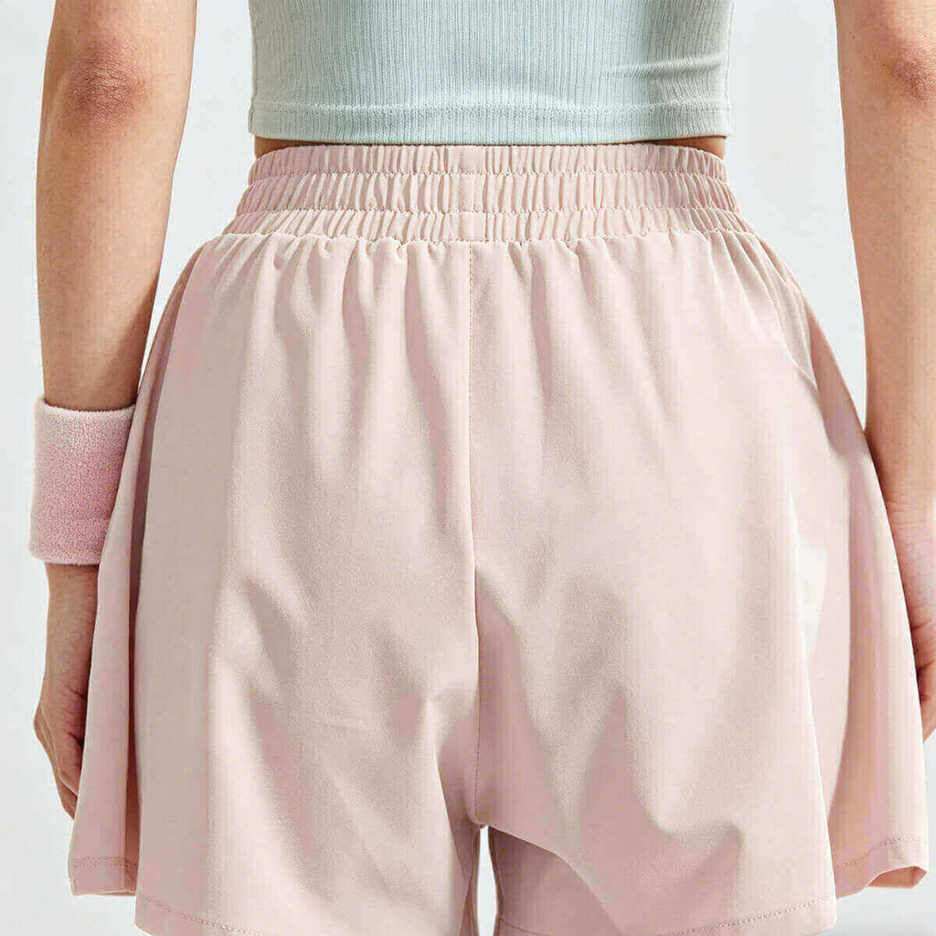Back view of flowy workout shorts for women in light pink, highlighting the flattering high-rise fit and breathable fabric for summer sports.