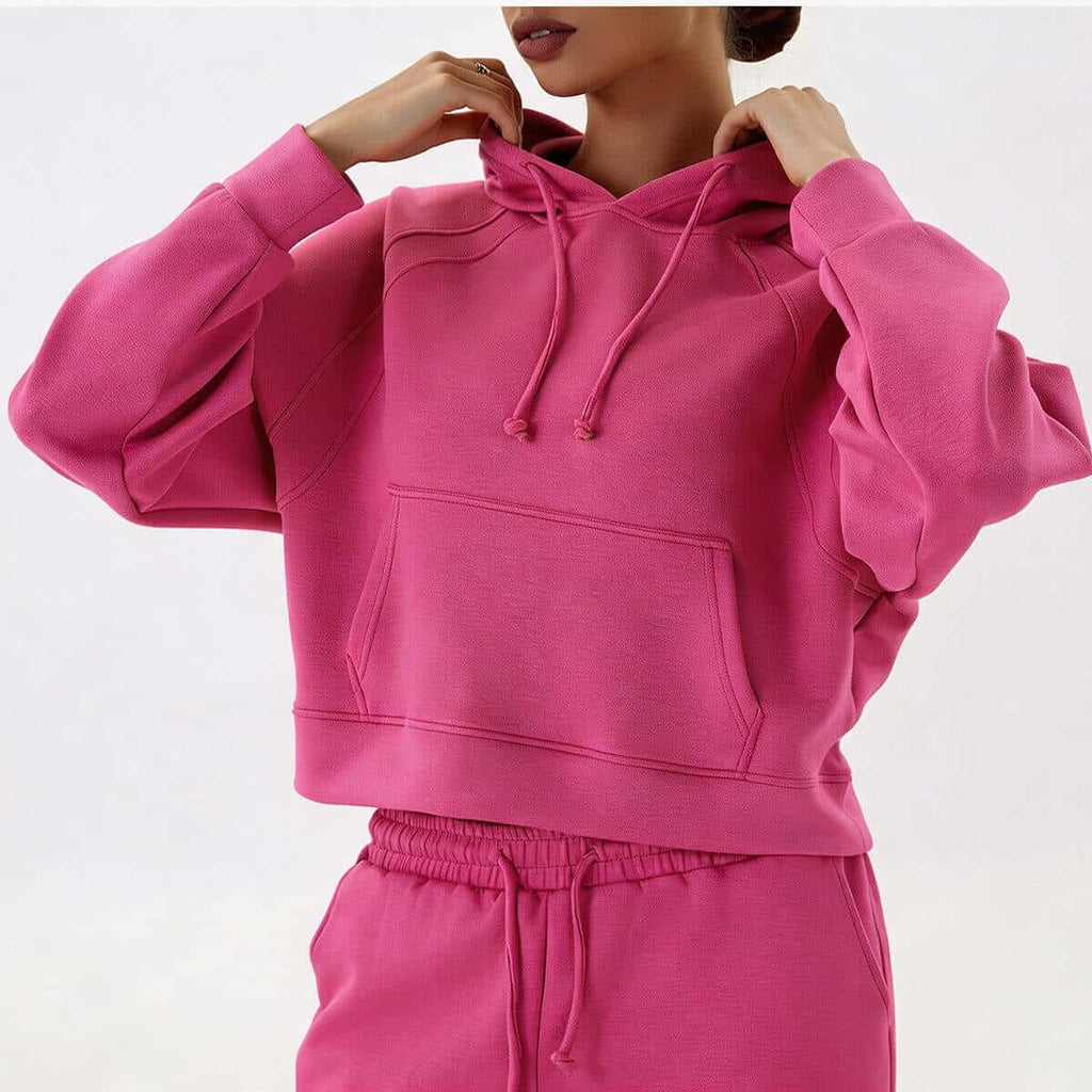 Detailed posing view of a fuchsia pink cropped pullover hoodie, highlighting the unique overlock stitching on the raglan sleeves.