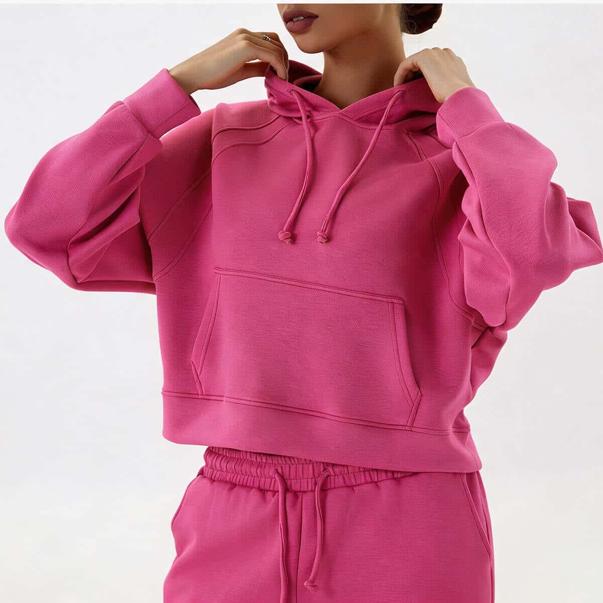Detailed posing view of a fuchsia pink cropped pullover hoodie, highlighting the unique overlock stitching on the raglan sleeves.