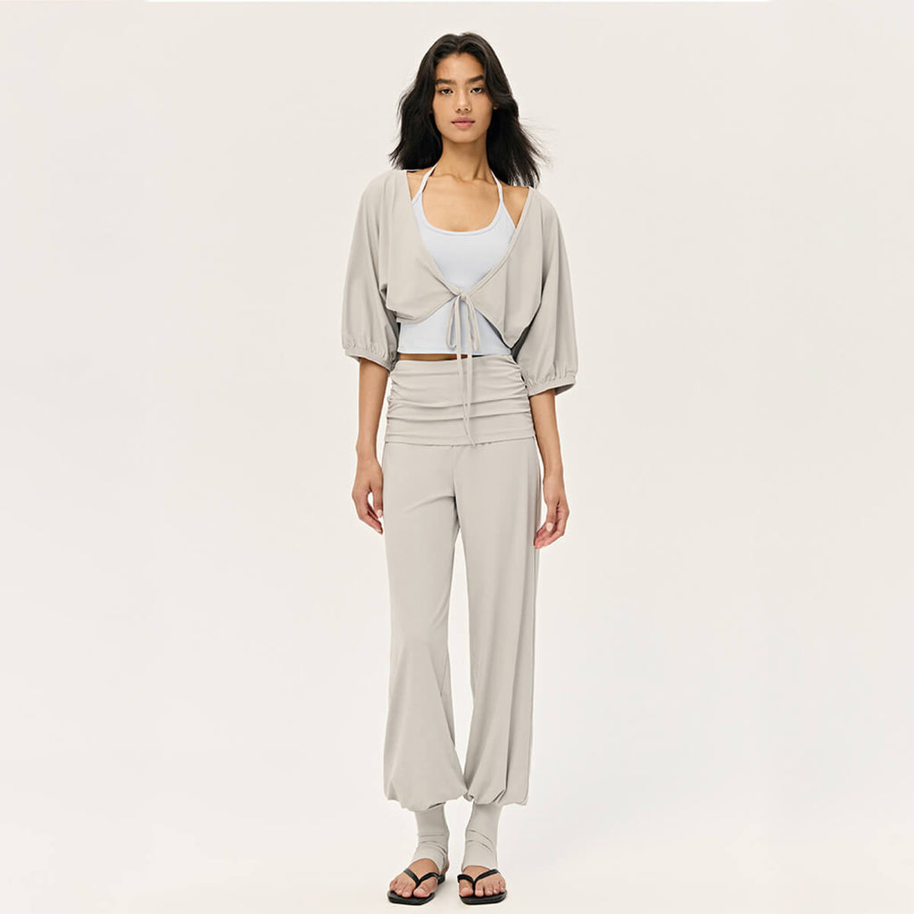 Full body view of a woman in a light grey balletcore activewear set, including a cropped shrug and wide-leg yoga pants.