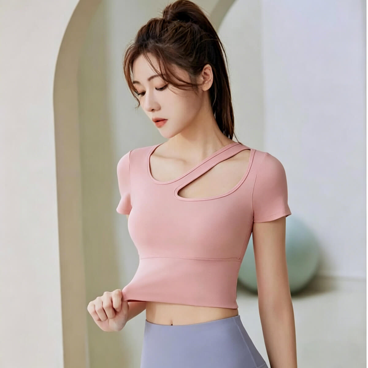 A dusty pink gym top with a cutout neck being stretched to demonstrate the high elasticity and durable performance material.