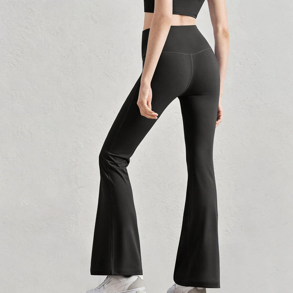 Rear view of a woman wearing black high-waisted flare leggings with a body-hugging fit and a flattering bell-bottom silhouette.