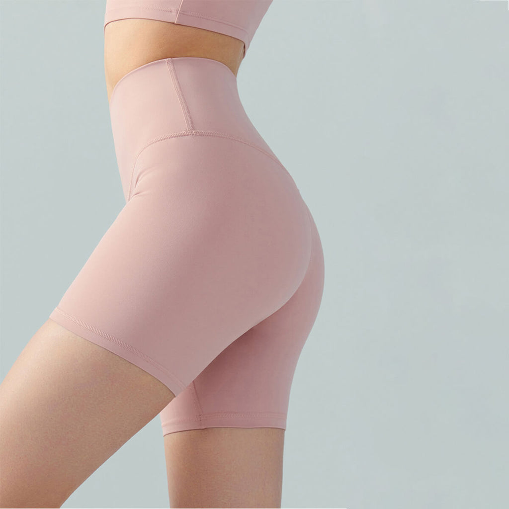 Close-up side view of a woman wearing high-waisted pink yoga shorts with a buttery-soft nude feel fabric and flattering fit.