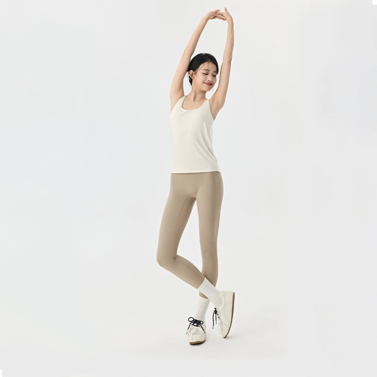 Front view of a woman in an ivory yoga tank top paired with khaki leggings and white sneakers for an athleisure look.