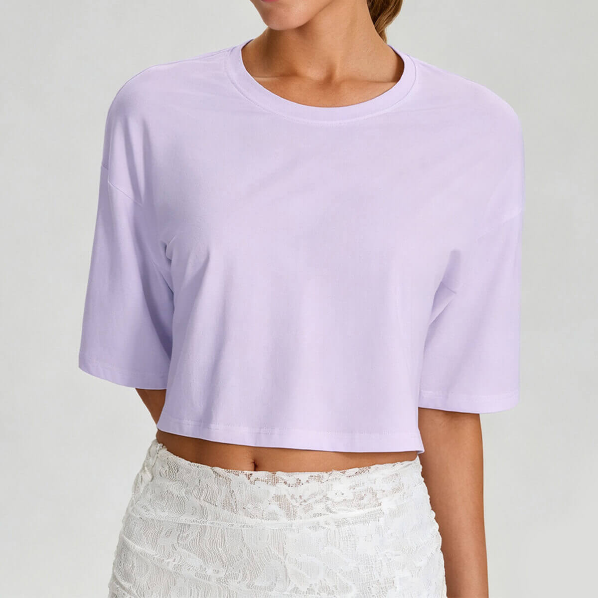A woman wearing a light lavender purple athletic crop t-shirt with a stylish drop shoulder design.