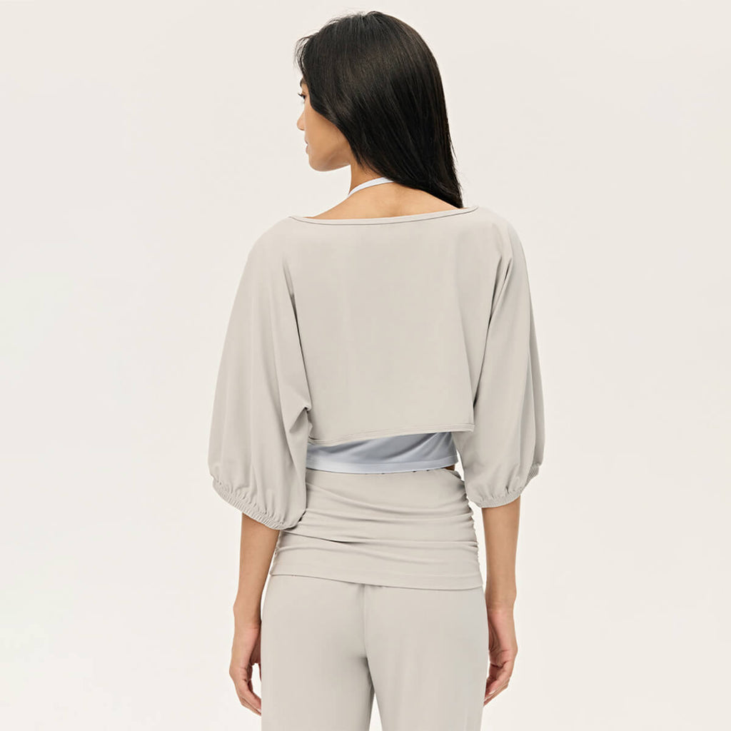 Rear view of a woman wearing a light grey cropped shrug, showcasing the loose fit and balloon sleeve design.
