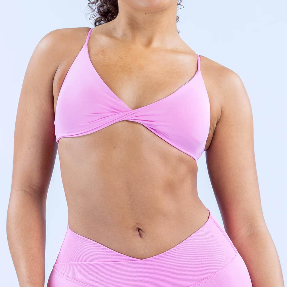 Woman wearing a light pink strappy sports bra with a flattering twist-front design for Pilates.