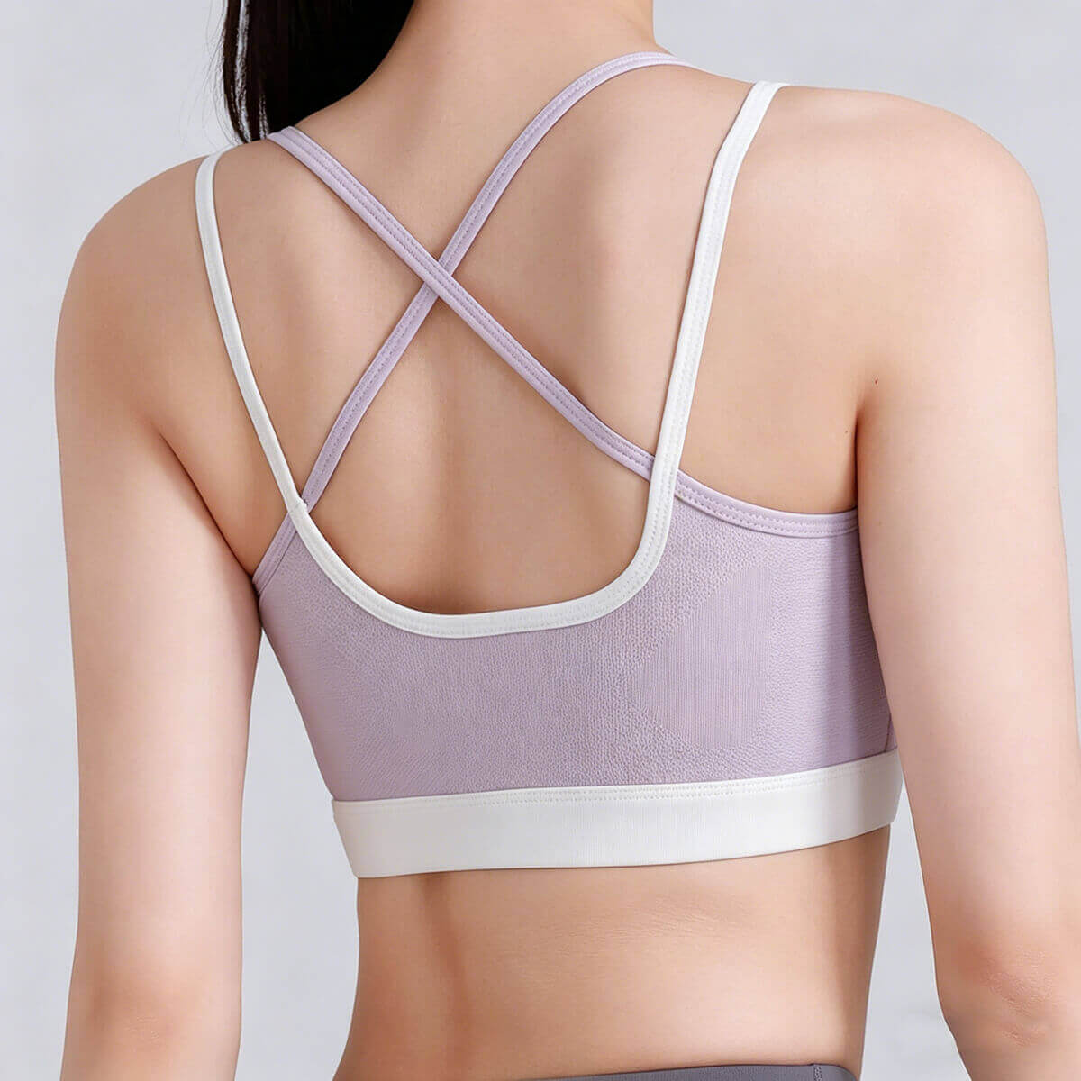 Back view of a lilac purple sports bra featuring textured performance fabric and a white criss-cross strap design for maximum breathability
