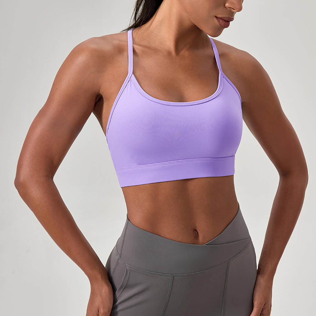 A woman wearing a lavender purple sports bra with thin straps, ideal for low-to-medium impact activities like Pilates.