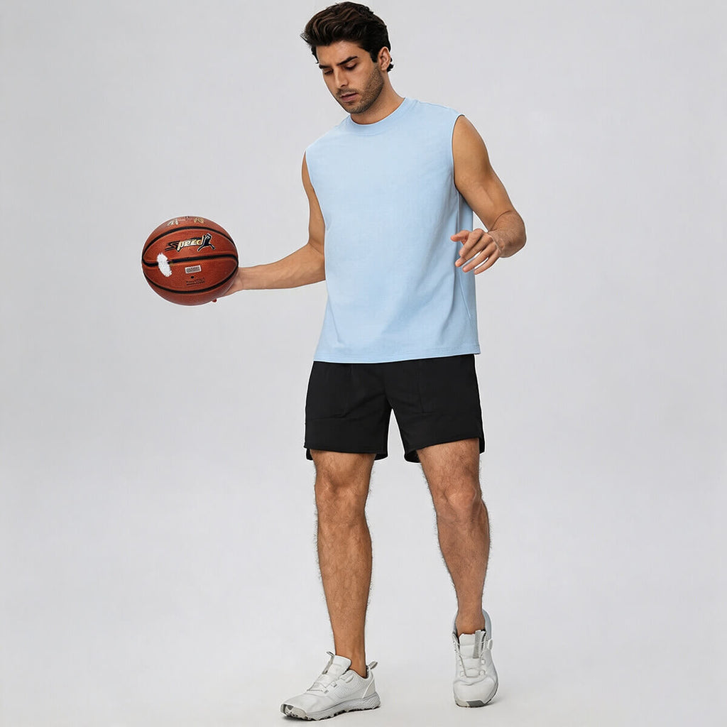 A man dribbling a basketball wearing a light blue sleeveless workout shirt and black athletic shorts.