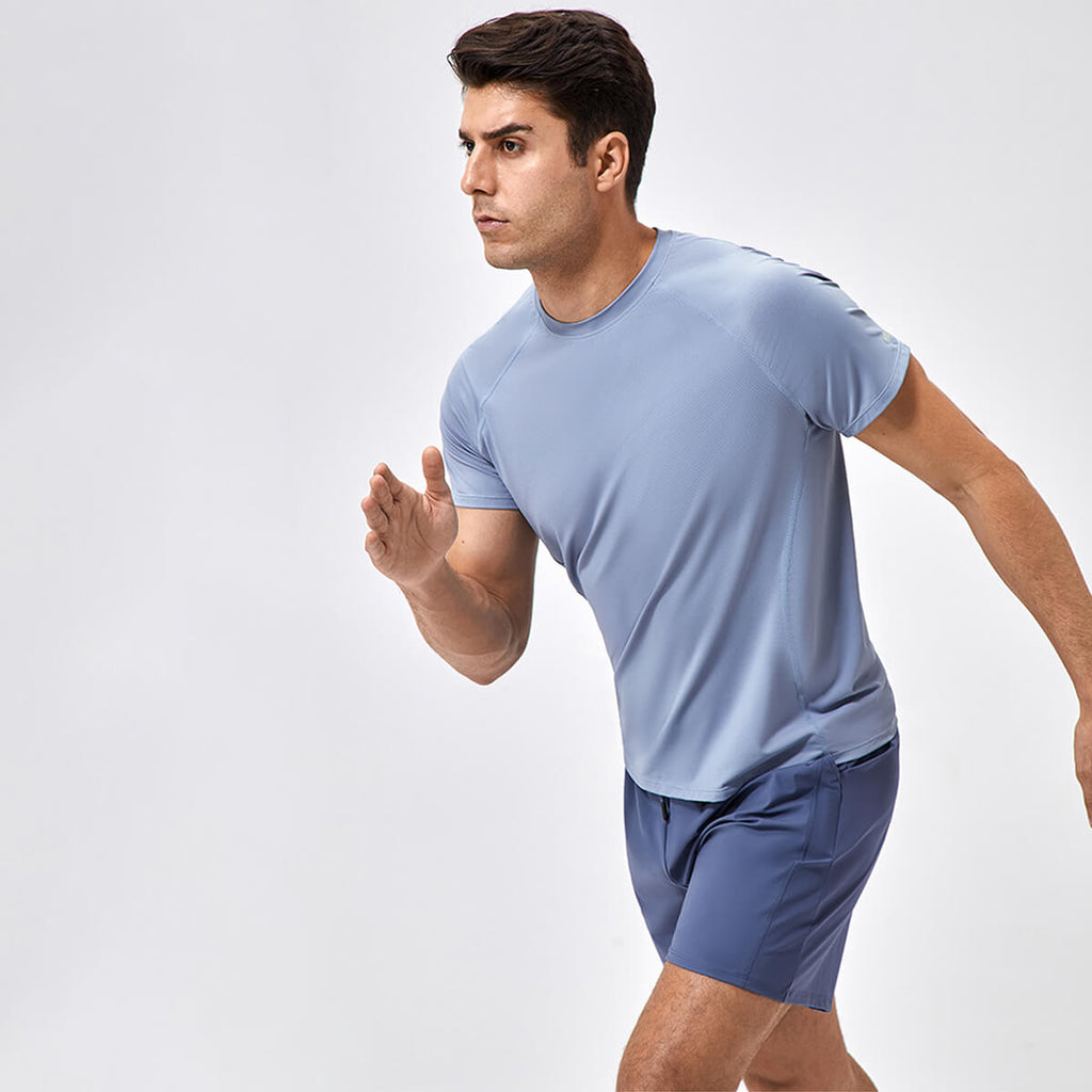 A man in a slate blue quick-dry running T-shirt demonstrating mobility during outdoor exercise.