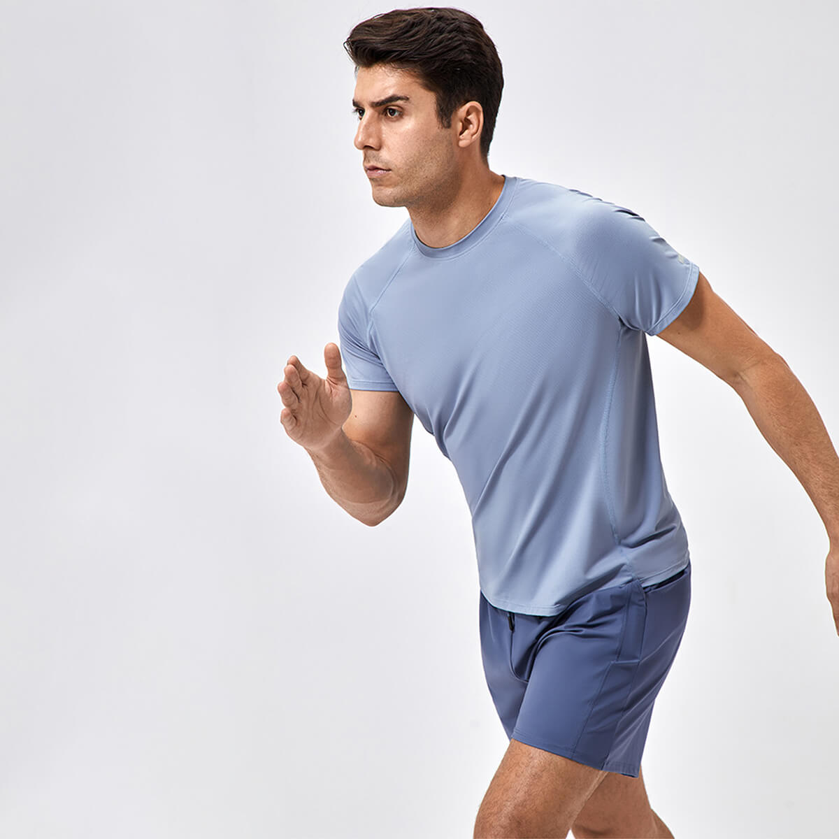 A man in a slate blue quick-dry running T-shirt demonstrating mobility during outdoor exercise.
