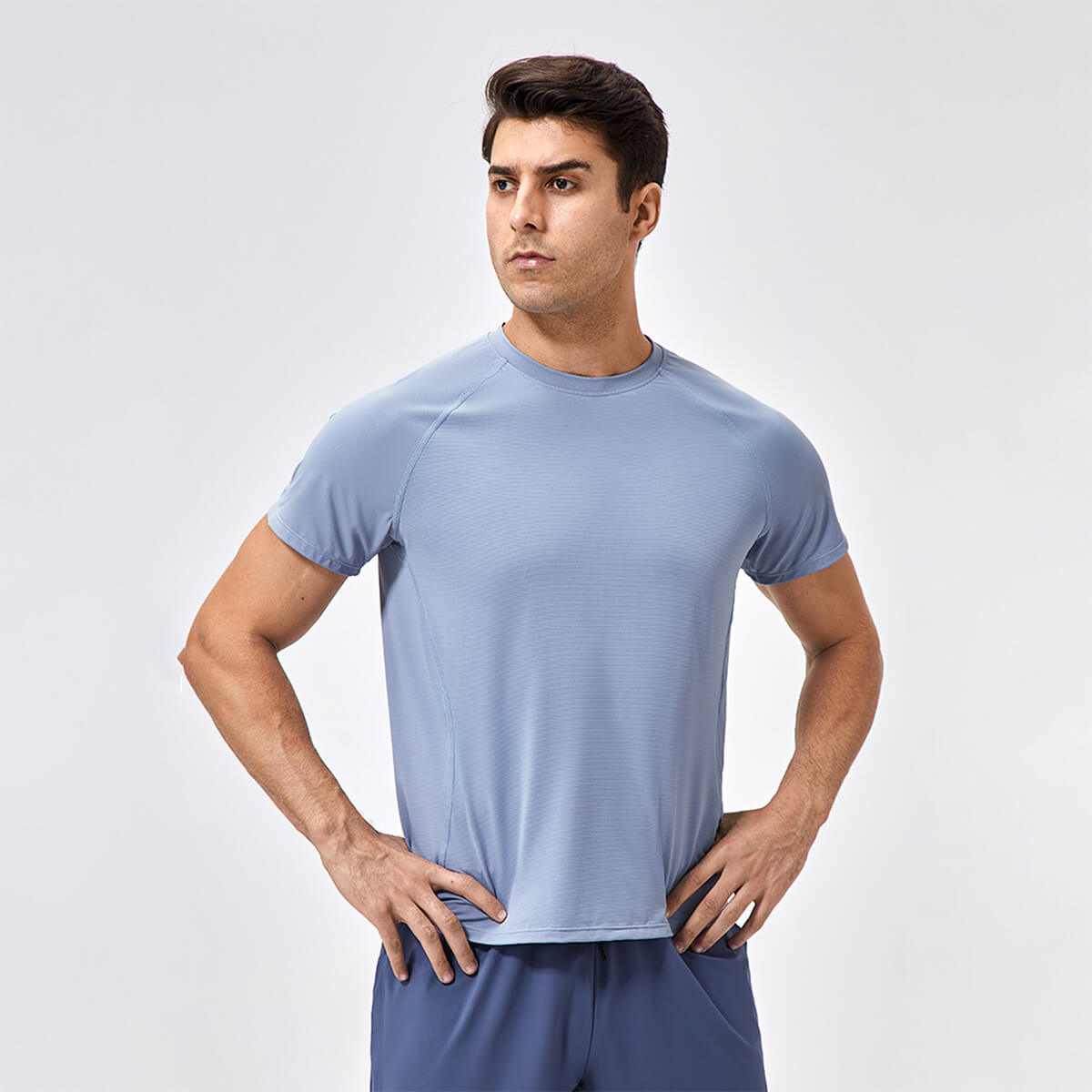 A man posing in a slate blue short-sleeve yoga and workout top with his hands on his hips.