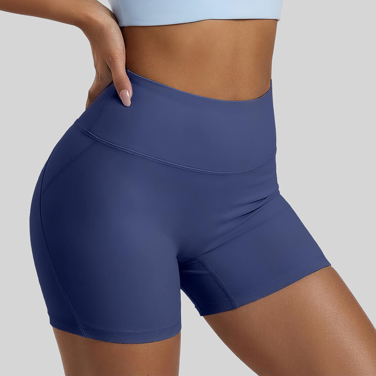 Close-up side view of a woman wearing navy blue high-waisted yoga shorts, featuring a supportive wide waistband and body-contouring seams for a flattering workout fit.