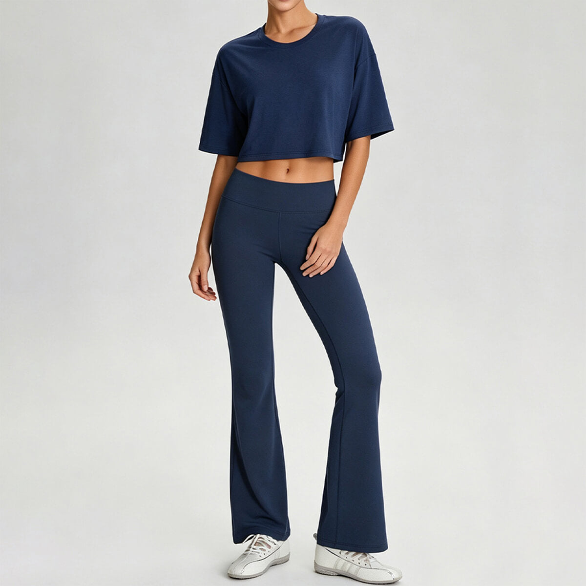 Full body view of a woman wearing a navy blue boxy cropped tee and matching flare yoga pants for an athleisure look.