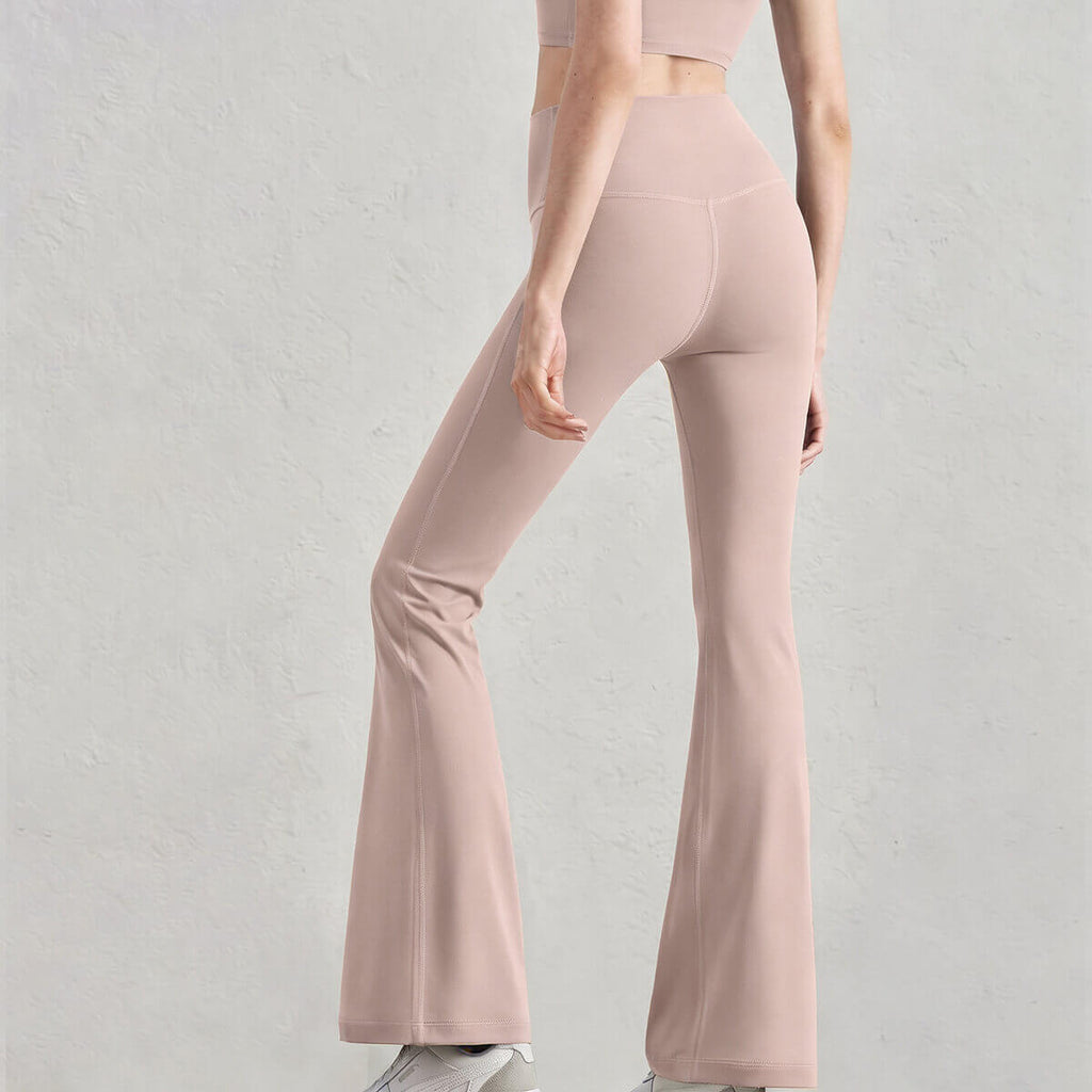 Rear view of a model in blush pink buttery soft flare yoga pants, highlighting the sleek and flexible athletic fabric.