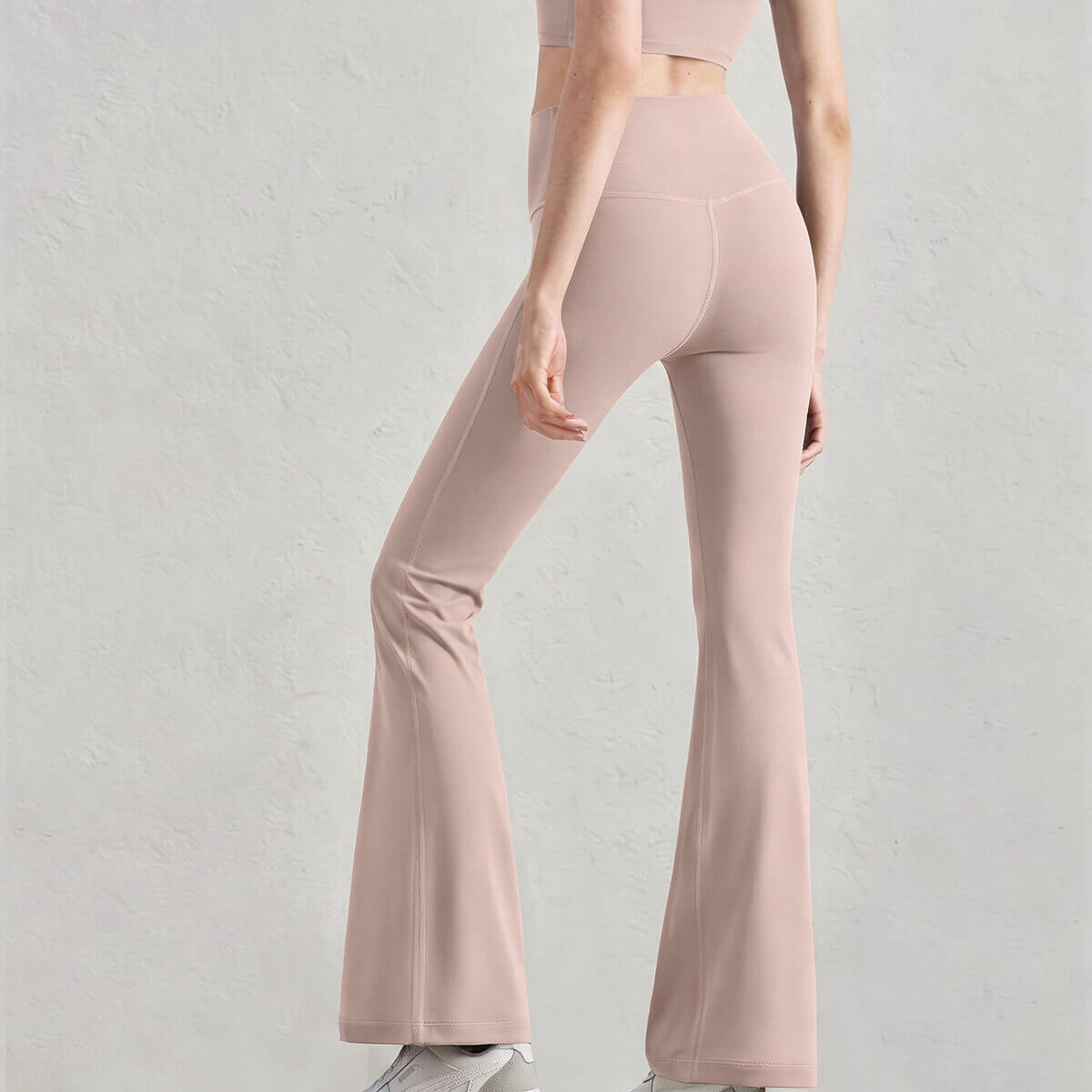 Rear view of a model in blush pink buttery soft flare yoga pants, highlighting the sleek and flexible athletic fabric.