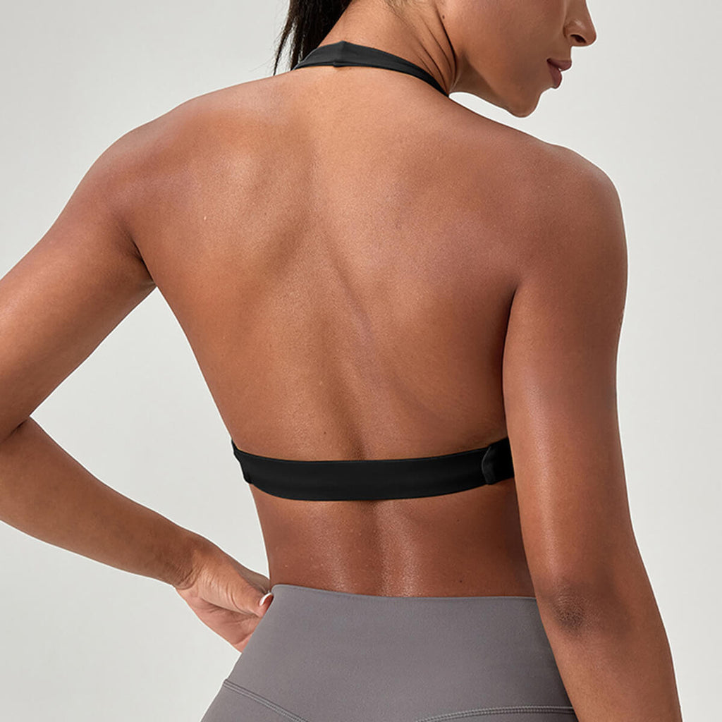 Back view of a black halter sports bra showcasing the wide elastic band and breathable open back design