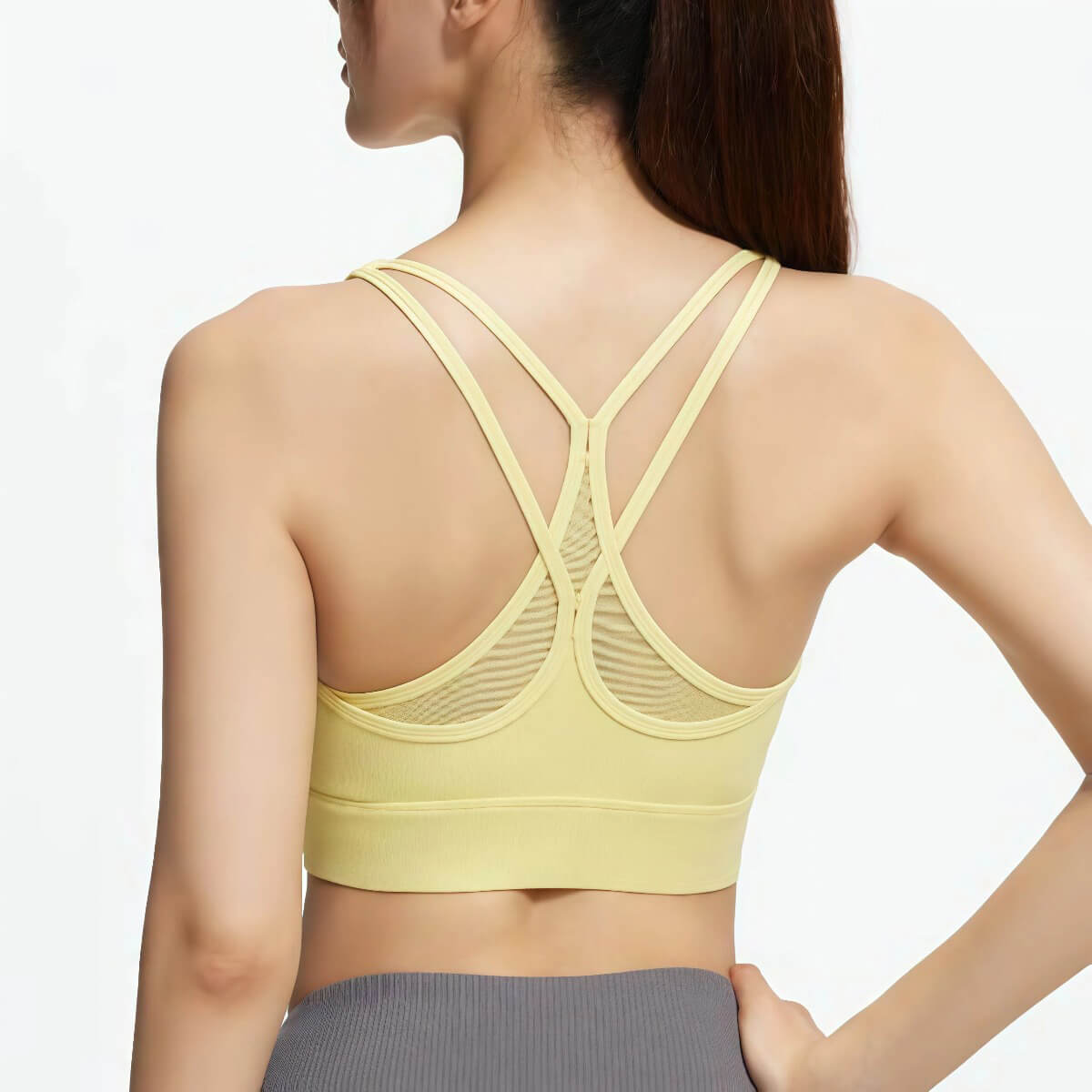 Back view of a pastel yellow racerback yoga bra with mesh inserts and supportive wide under-bust band for medium impact workouts