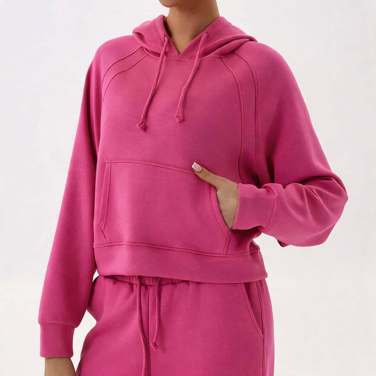 A woman in a vibrant hot pink 2-piece loungewear set, showcasing the trendy cropped hoodie and matching drawstring pants.
