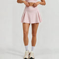 Front view of a woman wearing a light pink high-waisted pleated tennis skirt with built-in shorts for athletic performance.